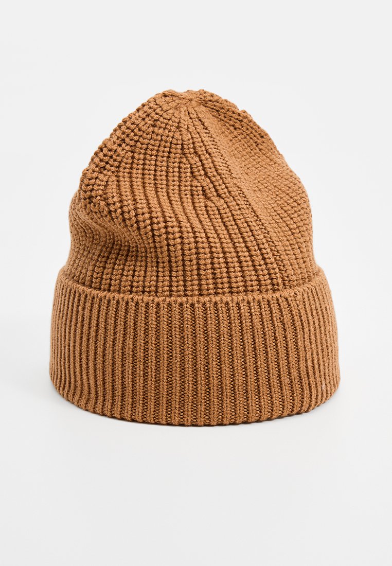 Brun stickad mössa med ribbad kant, texturerad kropp och något avsmalnande topp. Tyget verkar mjukt och flexibelt.