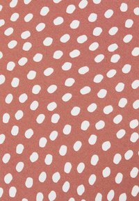 Tissu en couleur terracotta avec des pois blancs irréguliers. La surface semble douce avec une texture subtile.
