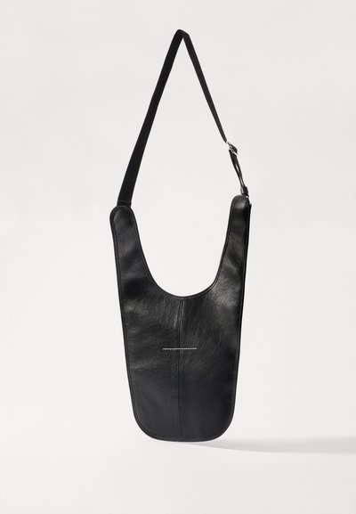 Borsa a spalla in pelle nera con una silhouette curva, lunga tracolla in tessuto e dettagli di cucitura bianca minimalista sulla parte anteriore.