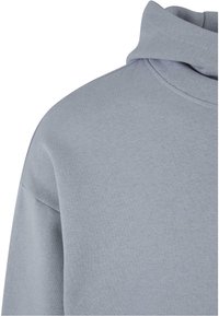 Sudadera gris clara con un cuello alto, textura suave y hombros anchos. La tela es lisa con un sutil detalle de costura a lo largo del escote.