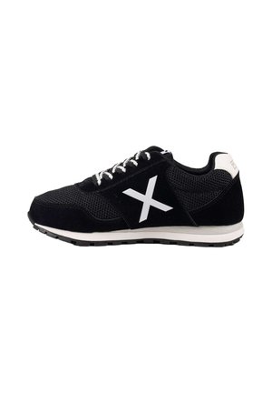 Zapatilla negra con cordones blancos, una gran X blanca en el lateral, detalle blanco en el talón y suela blanca con dibujo negro.