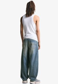 Hvid tanktop, løse blå denimjeans med en falmet finish og grå sneakers. Bagfra ses to lommer og en afslappet pasform.
