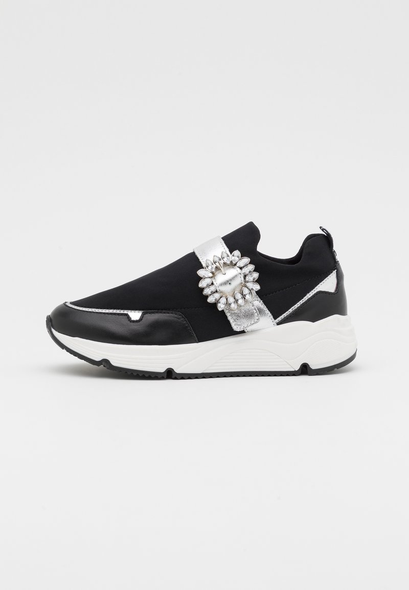 Baskets noires et argentées avec un col rembourré et une sangle décorative argentée ornée d'un accent en pierre précieuse ; semelle épaisse blanche ; matériaux lisses et texturés.