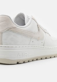 Vit lädersneaker med en texturerad mockaförslag, med en framträdande "AIR"-design på sulan och subtila perforeringar på tån.
