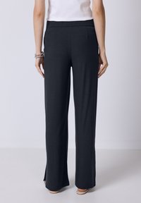 Pantaloni larghi a coste neri con vita alta, dotati di spacchi laterali all'orlo e una texture liscia. Il tessuto sembra traspirante.