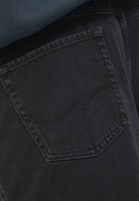 Czarna tkanina dżinsowa o teksturowanym wykończeniu, z tylną kieszenią ozdobioną zakrzywionym szwem, część dolnej części ubrania.