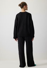 Black oversized knitted sweater with ribbed neckline and cuffs, paired with black wide-leg pants featuring a subtle leopard pattern.