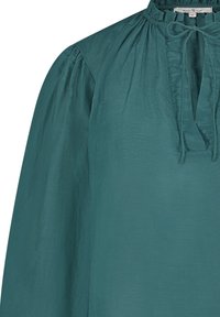 Teal blouse met een hoge hals, geplooide details en een strikfeature. Lange mouwen en lichtgewicht stof met een gladde textuur.
