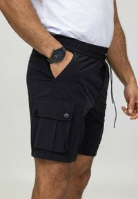 Shorts cargo noirs avec une taille élastique, dotés de poches latérales et de poches à rabat boutonnées. Fabriqués en tissu léger avec une texture lisse.