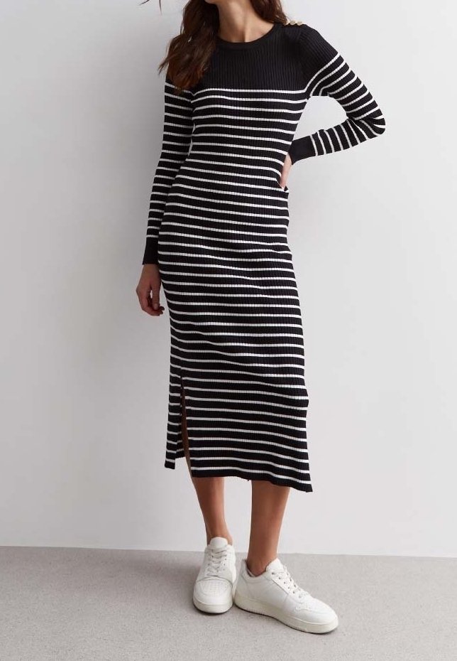 Femme portant une robe midi à manches longues rayée horizontalement en noir et blanc, fendue sur le côté, et des baskets blanches, debout avec une main sur la hanche.