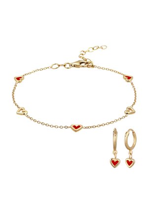 Guld kædearmbånd og matchende øreringe med røde emaljehjertevedhæng på hvid baggrund.