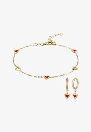 Bracelet chaîne en or et boucles d'oreilles créoles assorties avec des pendentifs en forme de cœur émaillés rouges sur fond blanc.