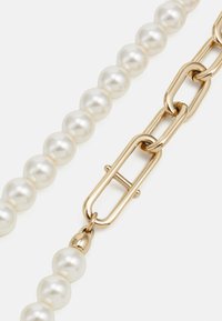 Perlenkette bestehend aus glänzenden weißen Perlen und goldfarbenen Metallverbindungen, mit einem Verschlussdetail für sicheren Halt.
