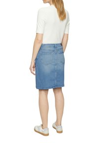 Leren rok in lichtblauw met een rechte snit, achterzakken en een klassieke tailleband. Gekleed met een witte top met korte mouwen en witte sneakers.