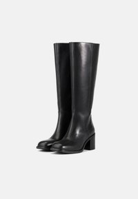 Botas de cuero negro hasta la rodilla con tacón cuadrado, textura suave, punta redonda y detalles de costura a lo largo de los lados.
