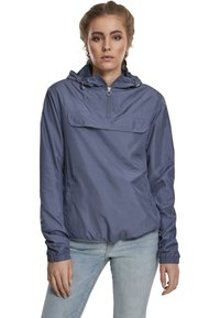 Giacca leggera con cappuccio di colore blu ardesia. Presenta una zip parziale sul davanti, polsini elasticizzati e tasca a marsupio con una texture liscia e lucida.