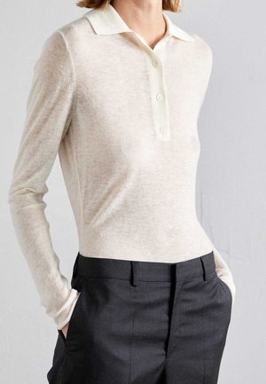Lange mouw polo in lichtbeige, met een knoopsluiting, zachte textuur en casual pasvorm, gecombineerd met donkere, op maat gemaakte broek.