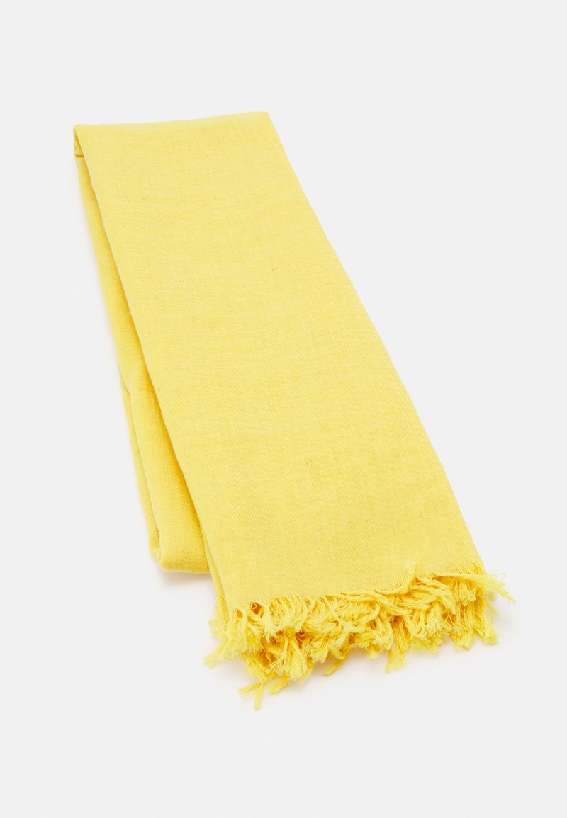 Écharpe jaune en tissu léger ; elle présente une texture douce et des bords frangés. Plissée à plat sur un fond blanc.