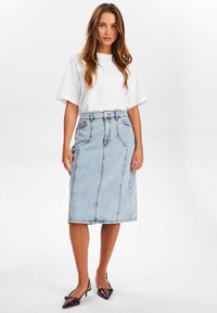 Svetlo modra jeans krila do kolen, z prednjimi šivi, visokim pasom in gumbnim zapiranjem. Usklajena s preprosto belo srajco s kratkimi rokavi.