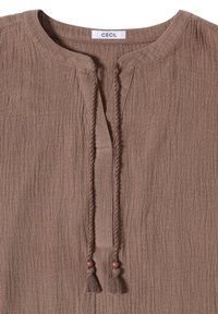 Tunique marron texturée avec encolure ronde, fente ouverte devant, liens à pampilles tressés avec perles, et une étiquette « CECIL » à l'intérieur du col.
