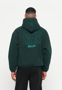 Green hoodie with a loose fit, featuring a graphic design on the back, elastic cuffs, and drawstring hood. Made from soft fabric.