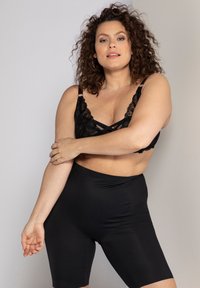 Bralette in pizzo nero con spalline incrociate e shorts modellanti neri a vita alta, caratterizzati da una texture liscia e un design aderente.