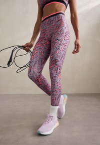 Stanik sportowy i legginsy w odcieniach szarości z różowymi abstrakcyjnymi wzorami. Długie rękawy, pasujące buty w jasnym fioletowym kolorze z pastelowymi akcentami. Regulowana skakanka.