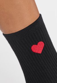 Calza nera a coste con un piccolo ricamo a forma di cuore rosso vicino alla parte superiore. La calza è morbida al tatto e aderente alla caviglia.