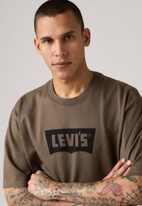 Olivgrünes Baumwoll-T-Shirt mit kurzen Ärmeln, das auf der Brust ein großes schwarzes Levi's-Logo trägt. Schlichte, lockere Passform mit Rundhalsausschnitt.