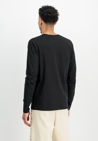 Camiseta de manga larga negra con cuello redondo, que presenta una textura suave y un diseño minimalista. Impresión de logo visible a lo largo de las mangas.