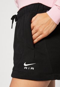 Černé šortky Nike s elastickým pasem na šňůrku a bočními kapsami. Na lemu je bílé logo "AIR" a swoosh. Měkká, strukturovaná tkanina.