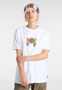 Hvid bomulds t-shirt med et farverigt sommerfugl grafik, en pink cirkel og sort tekst. Korte ærmer og en afslappet pasform.