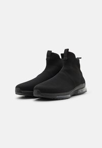 Černé slip-on tenisky s pleteným svrškem, které mají hladkou texturu, elastické detaily a průhlednou polstrovanou podešev.