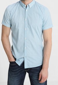 Camisa de botón de manga corta, color azul claro, con un pequeño patrón repetido; hecha de algodón; presenta un cuello clásico y un dobladillo recto.