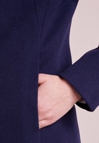 Navy wool coat with a smooth texture, featuring a side pocket and a tailored fit. The sleeve is slightly flared at the cuff.