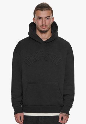 Black hoodie with a front pocket, featuring raised "DROPSIZE" text. Made from a soft fabric, it has a relaxed fit and adjustable drawstring hood.