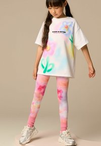 T-shirt bianco oversize con stampe floreali colorate e testo "BLOOM IN NATURE". I leggings abbinati presentano un motivo tie-dye rosa e pastello.