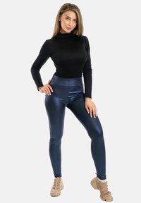 Top nero a maniche lunghe abbinato a leggins lucidi blu navy. L'outfit presenta una silhouette aderente e una texture liscia e riflettente.