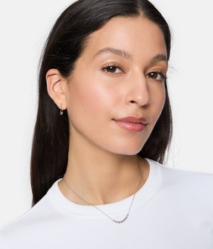 Silberne Kettenhalskette mit kleinen runden Details, getragen auf einem schlichten weißen T-Shirt. Einfache Creolen ergänzen den Schmuck.