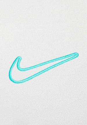 Logo de Swoosh de Nike bordado en turquesa claro, situado sobre un fondo de tela blanca suave. Diseño simple y limpio.