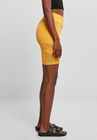Geel fietsbroek met een aansluitend ontwerp, voorzien van zijzakken en een gladde textuur. Gelijkend met zwarte sandalen en een cropped top.
