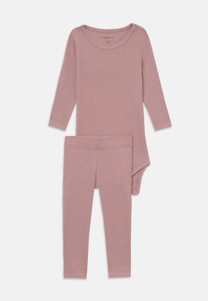 Hosszú ujjú bodysuit és leggings szett puha rózsaszín bordás anyagból. Kerek nyakkal és testhez simuló fazonnal rendelkezik, zökkenőmentes kialakítással.