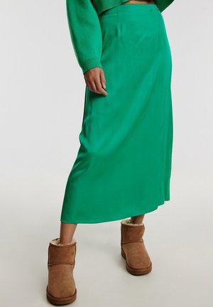 Groene, midi-lange rok van soepel, geweven stof met een eenvoudig, recht ontwerp. Gecombineerd met bruine, met schapenwol gevoerde enkellaarsjes.