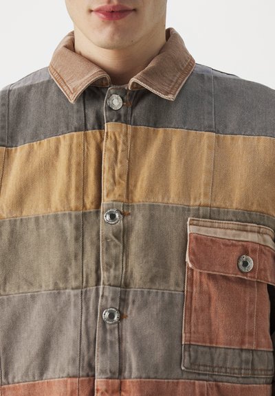 Patchwork-Jacke aus leichtem Stoff. Mit horizontalen Streifen in Beige, Grau und Rost, mit Druckknopfverschluss und einer Brusttasche.