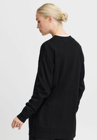 Pull noir oversize à manches longues, présentant une texture douce, un col rond et des coutures d'épaule abaissées, avec une coupe droite et un design minimal.