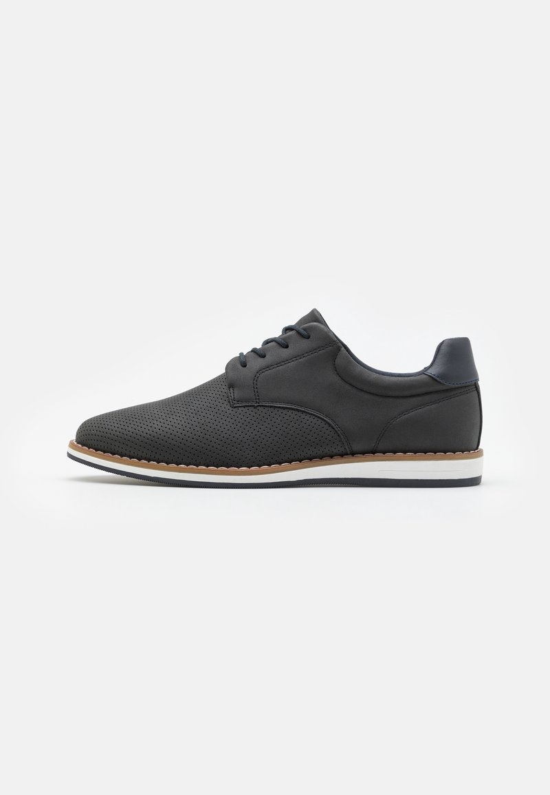 Chaussure décontractée noire à lacets avec embout perforé, col rembourré et semelle blanche bordée de marron, vue de profil sur fond blanc.