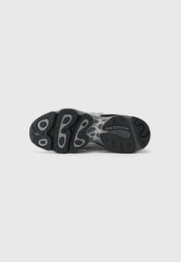 Black and grey sneaker sole with detailed tread patterns, featuring accents and branding on the bottom. Textured rubber material.