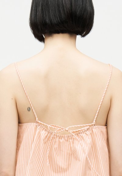 Άτομο με κοντά μαύρα μαλλιά που φοράει αμάνικο τοπ ριγέ σε ροδακινί και λευκό, με ορατή την πλάτη και ένα μικρό τατουάζ στην αριστερή ωμοπλάτη.