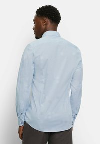 Helles, blaus Hemd mit kleinem, dunklem geometrischem Muster. Verfügt über einen klassischen Kragen, geknöpfte Manschetten und einen abgerundeten Saum.