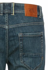 Jeans aus Denim in mittlerem Blau mit strukturierter Oberfläche, ausgestattet mit einem braunen Lederpatch mit "camel active" Branding und schrägen Gesäßtaschen.